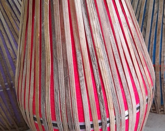Könnte beinhalten: Ein handgefertigtes indisches Percussion-Instrument, eine Mridangam, mit rotem Stoffinnenraum und einem gewebten Bambusäußeren. Die Trommel hat eine rötlich-braune Farbe und eine unverwechselbare Form. Weitere Trommeln sind im Hintergrund zu sehen.