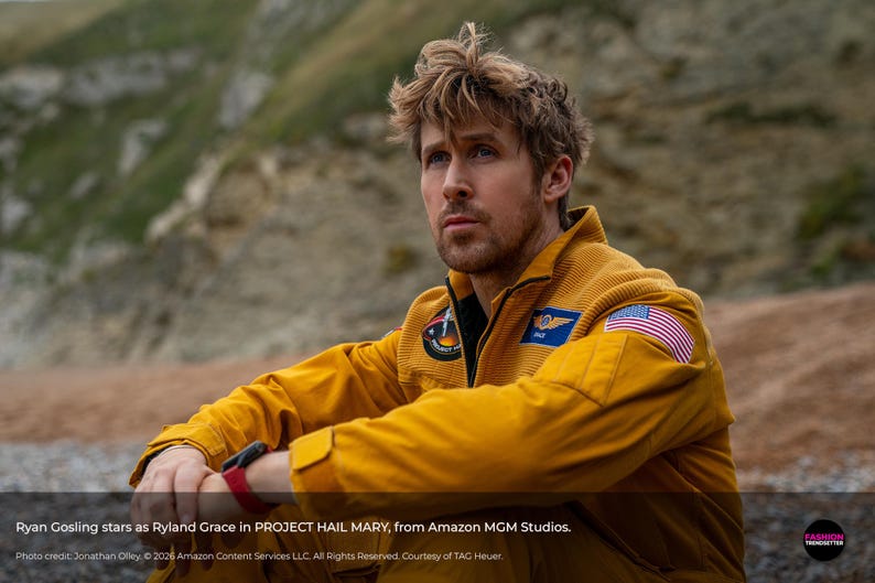 May include: A man wearing a mustard yellow jumpsuit with an American flag patch on the shoulder. The image includes text that reads "Ryan Gosling stars as Ryland Grace in PROJECT HAIL MARY, from Amazon MGM Studios."