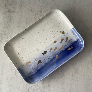 May include: Rectangular ceramic serving platter. The white surface is speckled, with a blue painted section. Gold fish swim across the blue area. The platter has rounded corners and a slightly raised edge.