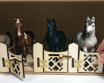 May include: A wooden stable with five horse figurines inside. The stable has a white wooden fence with a gate that opens. The horses are black, brown, white, and gray.