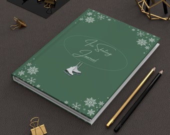May include: A green journal with the text "Ice Skating Journal" and a white snowflake design. The journal is lying on a brown surface with two pencils and gold paper clips.