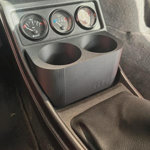 Puede incluir: Consola de salpicadero de automóvil negra con tres indicadores y dos portavasos. Los indicadores muestran la presión del aceite, la temperatura y otro indicador. El portavasos tiene las letras "GIII".