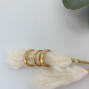 May include: Three gold wedding bands on a white fluffy background.