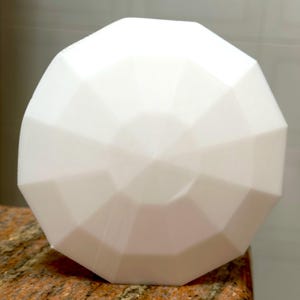 May include: A white, geometrically shaped, decorative object with a smooth, matte finish. The object has a rounded, dome-like shape with multiple facets.