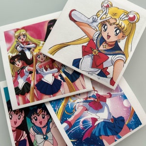 May include: Four square coasters featuring different images of Sailor Moon, a popular anime character. The coasters are white with a glossy finish and feature colorful images of Sailor Moon in various poses.