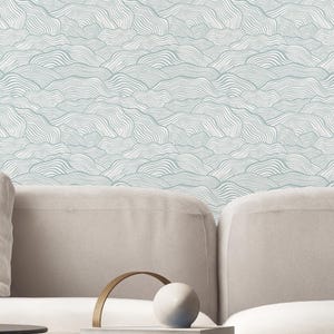 Puede incluir: Papel pintado con un patrón repetitivo de líneas onduladas en azul claro y blanco que recuerdan a colinas o nubes. El diseño consiste en trazos finos, continuos y de estilo dibujado a mano que crean un efecto texturizado y superpuesto.
