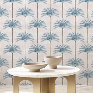 May include: A circular white table with a gold base holds two beige ceramic bowls. The backdrop showcases a repeating pattern of blue palm trees on a light beige textured surface, creating a tropical theme.