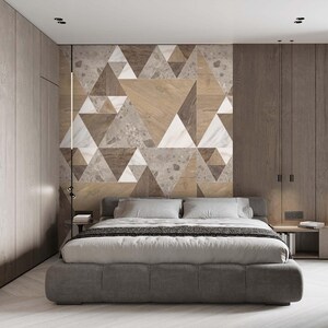 May include: A modern bedroom featuring a gray upholstered bed with white bedding and pillows. The headboard wall has a geometric design of triangles in wood, marble, and stone. Wooden cabinets and a side table complete the room's design.