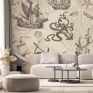 May include: A beige nautical-themed wallpaper featuring detailed illustrations of sailing ships, compasses, anchors, and an octopus. The design is in shades of brown and beige, creating a vintage aesthetic. The wallpaper is installed in a living room setting.