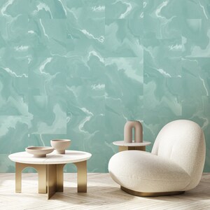 May include: A white, plush, modern armchair with a rounded, organic shape sits in front of a teal blue wall with a marbled pattern. A small, round, gold-toned table with a white top sits in front of the chair. A small, beige, abstract sculpture sits on the table.