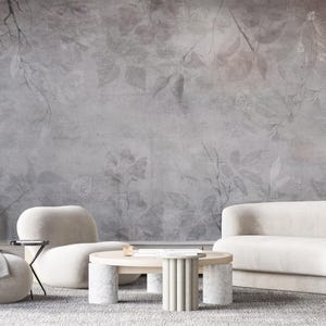 May include: A modern living room with a gray floral wallpaper backdrop. The room features a white sofa, a rounded armchair, and a round coffee table with a marble base. A small side table and a footstool are also present.