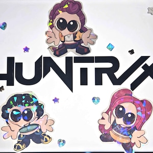 May include: White background with the word "HUNTRX" in bold black letters. Three cartoon character stickers with large eyes and holographic accents are scattered around the text, along with iridescent star and heart-shaped embellishments.