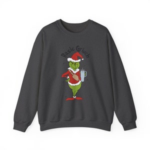 May include: A dark gray sweatshirt with a green Grinch character wearing a Santa hat and holding a cup. The text "Basic Grinch" is printed above the character.