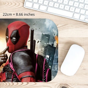 May include: A red and black Deadpool character mouse mat with a city skyline background. The character is holding a finger to his lips, as if to say "shhh". The mouse mat measures 22 cm by 18 cm.