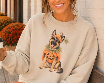 May include: A beige crewneck sweatshirt featuring a graphic illustration of a German Shepherd dog wearing a pumpkin costume with a matching hat. The dog is sitting and facing forward. The sweatshirt has long sleeves and a relaxed fit.