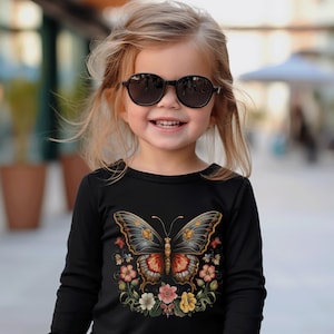 May include: A young girl wearing black sunglasses and a black long-sleeved shirt with a colorful butterfly graphic and floral accents.