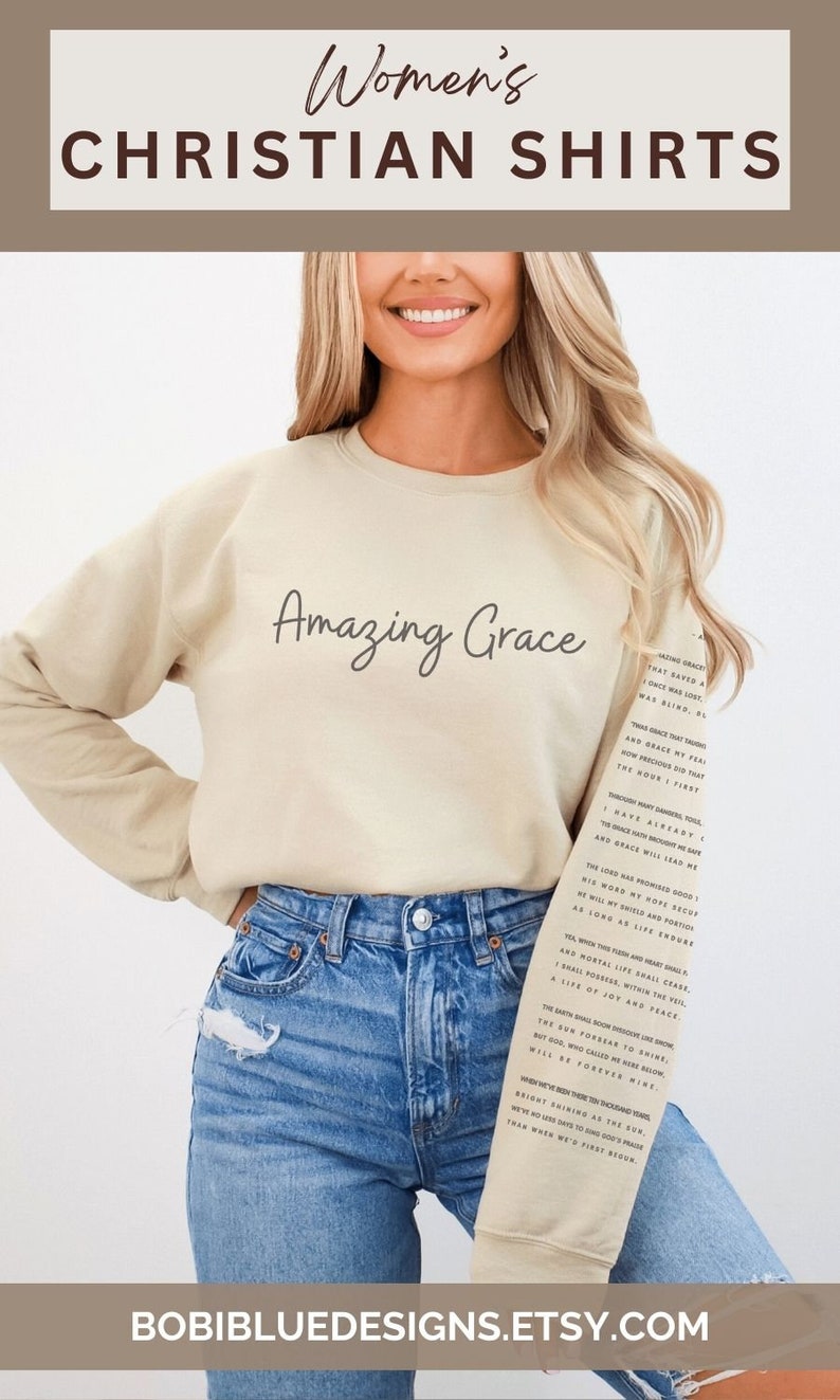 Op de afbeelding: Een beige sweatshirt met de tekst "Amazing Grace" erop gedrukt. De tekst staat in een cursief lettertype. Het sweatshirt wordt gedragen door iemand met blond haar en een blauwe jeans. De tekst van het kerklied "Amazing Grace" is op het sweatshirt gedrukt.
