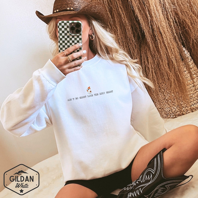May include: White crew neck sweatshirt with the text "AIN'T NO GHOST LIKE THE HOLY GHOST" in black. The sweatshirt features a small graphic of a chicken. The Gildan White logo is visible in the bottom left corner.
