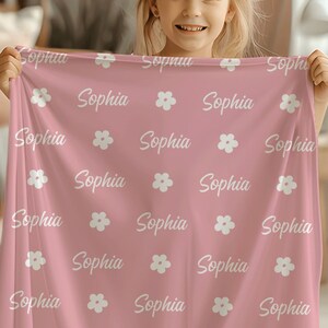 May include: A pink personalized blanket with a white floral pattern and the name "Sophia" repeated throughout.