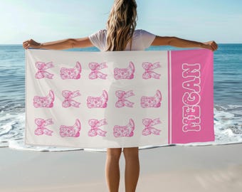 May include: A white beach towel with a pink border and a pink pattern of bows and shoes. The name "MEGAN" is written in pink on the towel.
