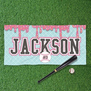 May include: A blue and white baseball themed towel with pink frosting and sprinkles. The towel has the name "JACKSON" in black letters and a baseball with the number "#3" on it.