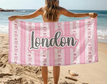 May include: A pink beach towel with a white and pink pattern of bows and lace. The word "London" is written in gray across the middle of the towel.