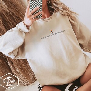 May include: A beige sweatshirt featuring the phrase "Ain't No Ghost Like The Holy Ghost" in black text, with a small ghost graphic. The sweatshirt is a Gildan Sand brand. The sleeves are long and the fit is relaxed.