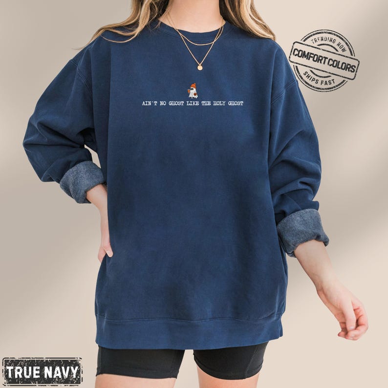 May include: A navy blue sweatshirt with the text "AIN'T NO GHOST LIKE THE HOLY GHOST" and a small graphic. The sweatshirt is a Comfort Colors brand. The sleeves are rolled up.