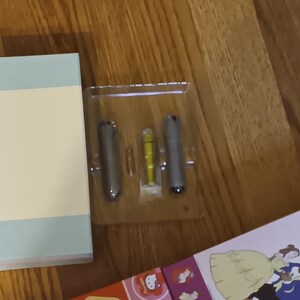 May include: A rectangular box in light blue and cream sits beside a clear plastic tray holding three silver and yellow objects. A colourful box with cartoon characters is partially visible.