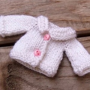 Puede incluir: Un cárdigan blanco de punto con cuello y dos botones rosas.