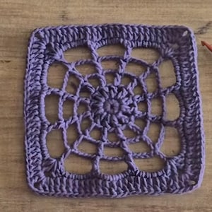 May include: A purple crochet square with a detailed, intricate design in the center. The square is made with a single crochet stitch and has a textured, woven appearance.