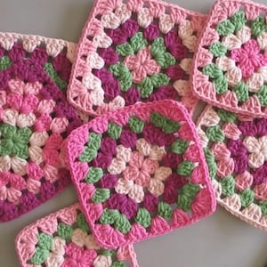 Puede incluir: Una colección de cuadrados de granny crochet en rosa, verde y blanco. Los cuadrados están hechos con una variedad de puntos y tienen un aspecto delicado y femenino.