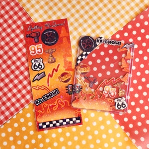 Könnte beinhalten: Zwei rote und orangefarbene Aufkleberbögen mit Cars-Motiv. Die Aufkleber zeigen die Figuren Lightning McQueen und Mater. Die Aufkleber enthalten den Text "Lighting McQueen!" und "Ka-Chow!"