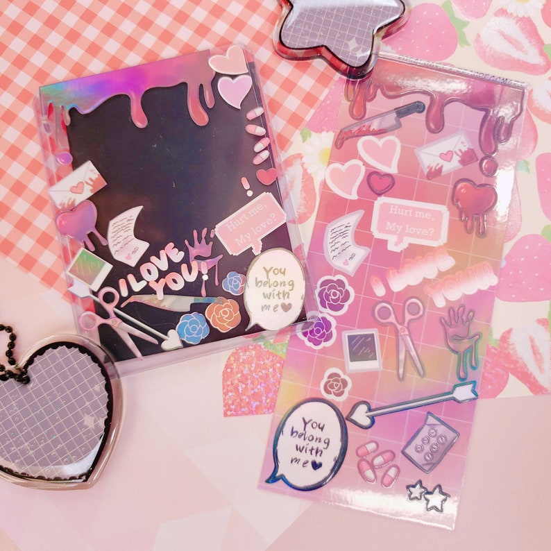 May include: Two clear plastic photo albums with colorful stickers and text. The text on the stickers includes "Hurt me, My love?" and "You belong with me".
