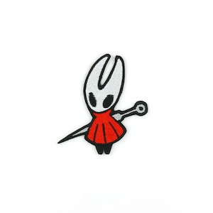 Peut inclure: Un patch brodé représentant un personnage du jeu vidéo Hollow Knight. Le personnage est blanc avec des vêtements rouges et tient une épée.