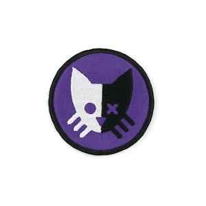 Può includere: Un cerotto rotondo viola con un designo di gatto bianco e nero. Il viso del gatto è diviso a metà, con un lato bianco e l'altro nero. Il lato bianco ha un punto nero per l'occhio e il lato nero ha una X per l'occhio.