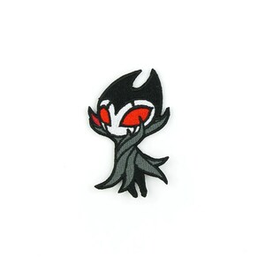 May include: Black and grey embroidered patch of a cartoon character with red eyes. The character has a pointed head and a long, flowing beard.