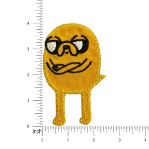Op de afbeelding: Gele geborduurde strijkpatch van een cartoonhond met een zonnebril en een grijns. De hond heeft zwarte ogen en een zwarte neus. De patch is ongeveer 5 cm hoog.
