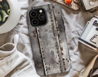 May include: A smartphone case with a distressed metal design. The case has a gray, industrial aesthetic with visible rivets and a textured surface. The case is designed to fit a modern smartphone with a multi-lens camera.