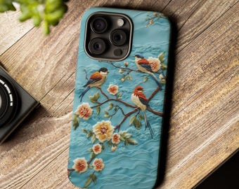 May include: A teal phone case featuring a detailed relief design of birds perched on flowering branches. The case has a textured background and a camera lens cutout. The birds have orange, blue, and black feathers. The flowers are peach and yellow.