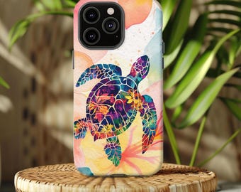 May include: A colorful phone case featuring a sea turtle design. The turtle is depicted with vibrant hues of blue, purple, and yellow, set against a watercolor background of pink, orange, and blue. The case is displayed on a woven wicker stand.