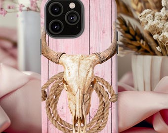 May include: A phone case featuring a bull skull with horns and a coiled rope design. The background is a pink, vertical wood-grain pattern. The case is designed for a smartphone.