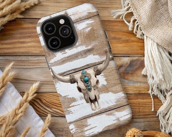 May include: A phone case featuring a cow skull design with turquoise accents. The case has a distressed wood background with white paint strokes. The phone case is on a wooden surface with decorative elements.