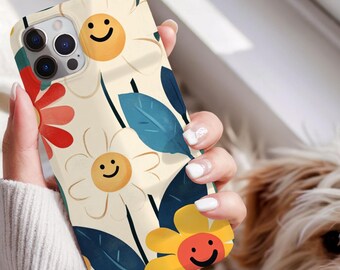 May include: A phone case with a floral design featuring smiling yellow flowers, red and yellow flowers, and blue leaves on a cream background. The case has a camera cutout and is held by a person.