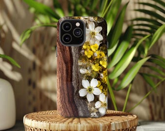 May include: A phone case with a wood grain design and embedded white and yellow flowers. The case has a dark brown wood grain pattern on the left side and a clear resin with flowers on the right.