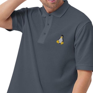 Peut inclure: Un polo bleu foncé avec un petit pingouin brodé sur la poitrine gauche. Le pingouin est noir et blanc avec un bec et des pieds jaunes.