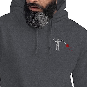 May include: Dark gray hoodie with a white skeleton flag design on the chest. The flag features a skeleton holding a spear, with a red heart and blood splatter. The hoodie has a drawstring hood.