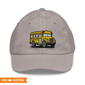 May include: A grey baseball cap with an embroidered yellow school bus design. The school bus has black tyres and windows, with red and yellow accents. The cap has a curved peak and a six-panel design.