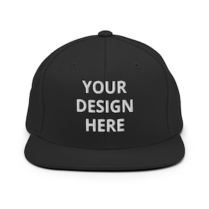 May include: Black flat-brimmed baseball cap with the embroidered text "YOUR DESIGN HERE" in white. The cap has a structured fit and a rounded crown. A classic accessory for casual wear.