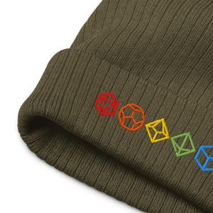 May include: Olive green beanie with embroidered colorful dice shapes. The beanie features a ribbed knit texture and a row of embroidered dice in red, orange, yellow, green, and blue.